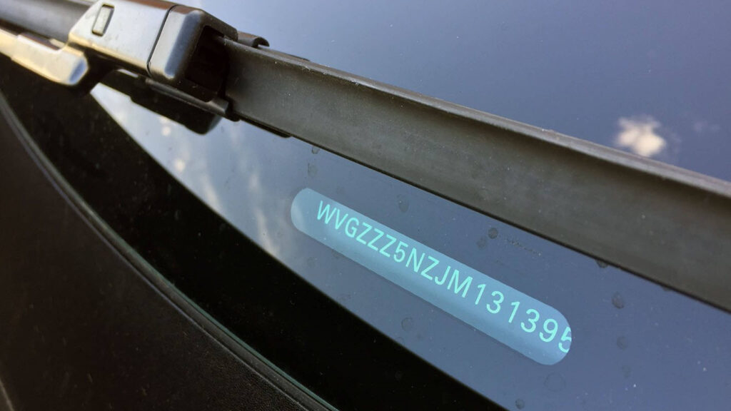 Detail čelního skla automobilu s nálepkou obsahující identifikační číslo vozidla (VIN), které je 'WVGZZZ5NZJM131399', odrážející se v skle.