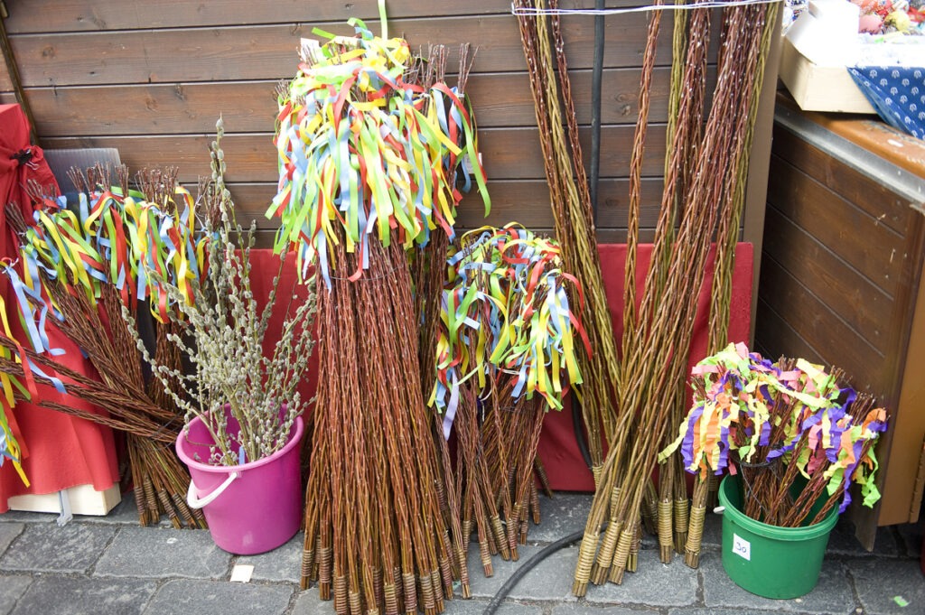 Velikonoční pomlázky s pestrobarevnými stuhami, tradiční české velikonoční proutěné bičíky, jsou vystaveny společně s větvemi kočiček v kbelících na trhu.