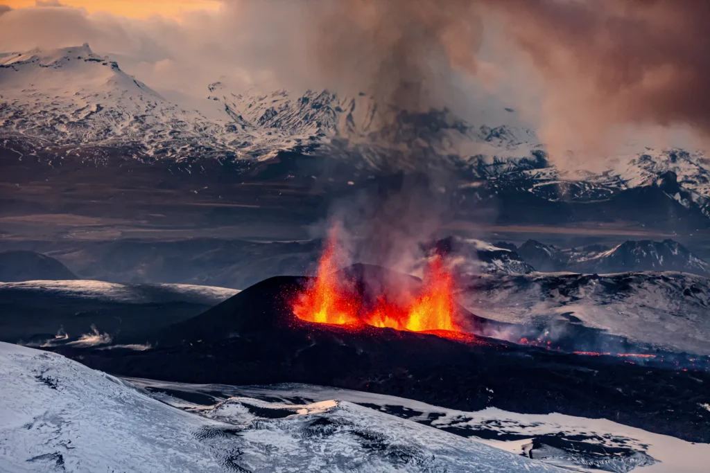 Erupce sopky Eyjafjallajökull s výtrysky lávy protínající chladné islandské krajiny pokryté sněhem a ledem, s dramatickým dýmem míchajícím se se západním světlem.