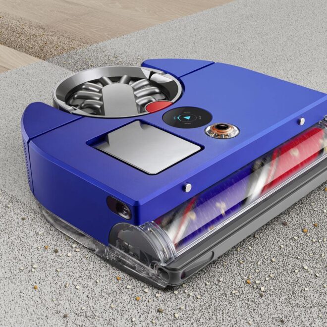 Modrý robotický vysavač Dyson při práci na koberci a tvrdé podlaze, se zametaným odpadem.