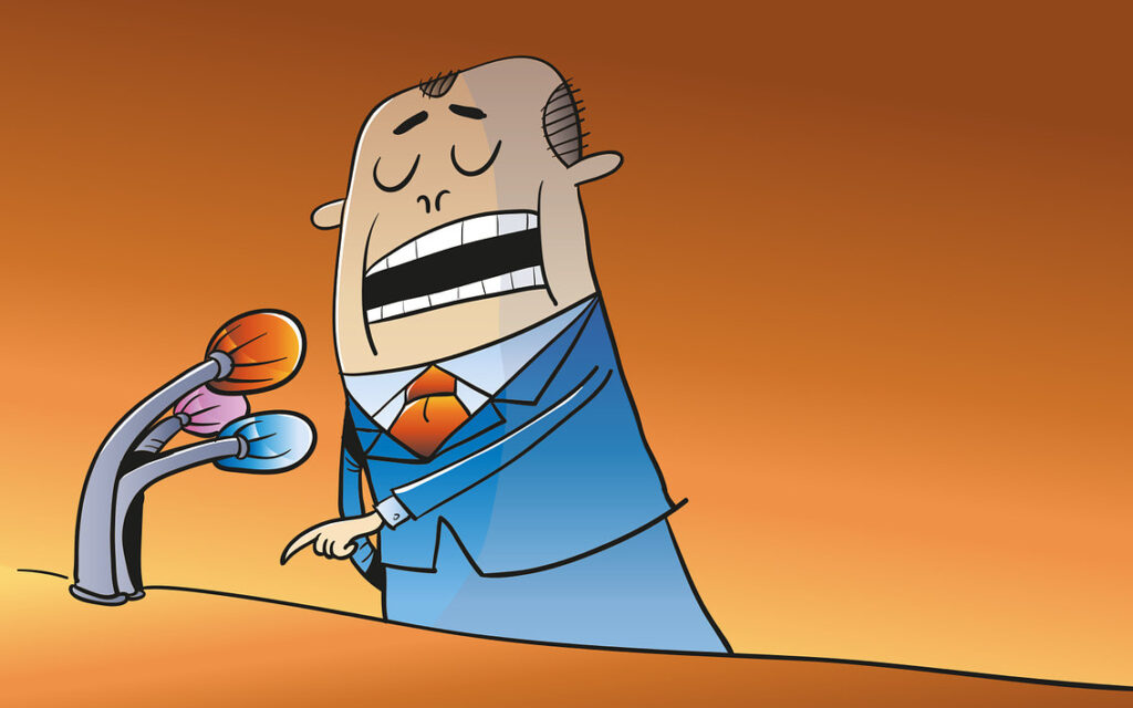 Karikatura politika v modrém obleku s oranžovou kravatou, který mluví do tří mikrofonů. Politika má zavřené oči a výrazně gestikuluje. Pozadí je oranžové.