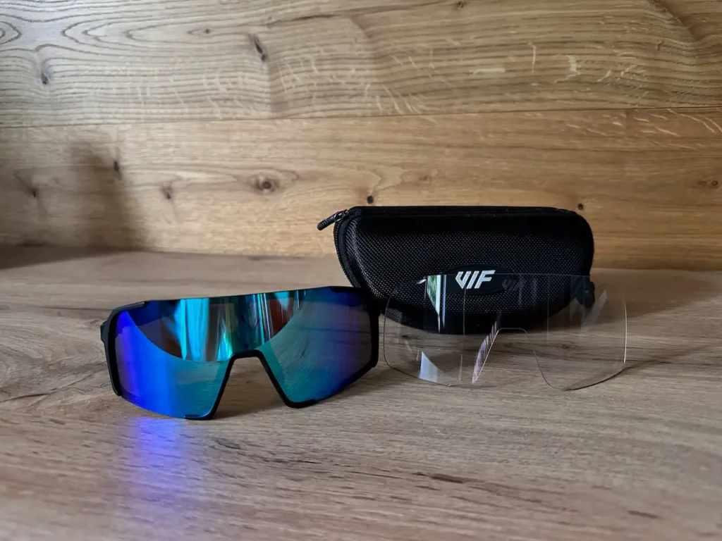 Brýle Vif Black X Ice Blue s modrými polarizačními čočkami, pouzdrem a náhradními čirými čočkami na dřevěném povrchu.