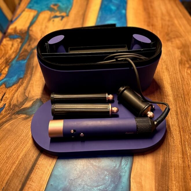 Sada Multistyler Dyson Airwrap Complete Long v elegantní fialové barvě uložená v ochranném pouzdru, umístěném na dřevěném stole s modro-fialovou epoxidovou říčkou.