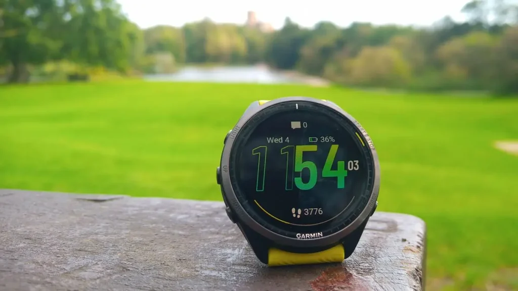 Sportovní hodinky Garmin Forerunner 965 položené na stole s výhledem na zelený park v pozadí.