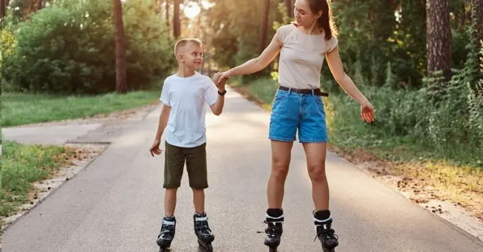 Žena a chlapec bruslí mají kolečkové brusle po silniční cestě. Drží se za ruce a užívají si společnou venkovní aktivitu za slunečného dne.