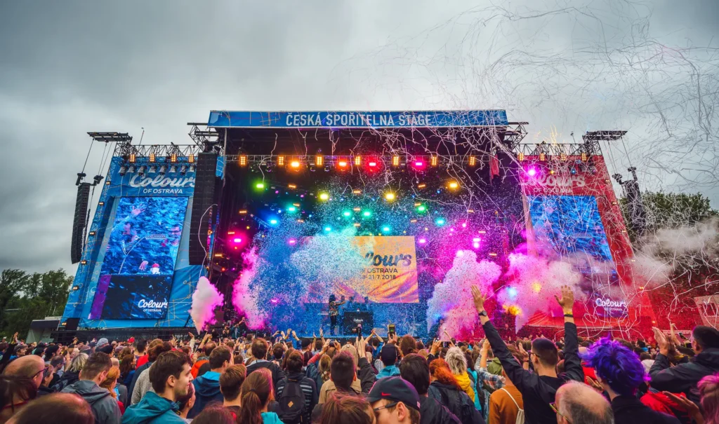 Pódium na festivalu Colours of Ostrava 2018 s barevnými světly a konfety, obklopené davem nadšených návštěvníků.