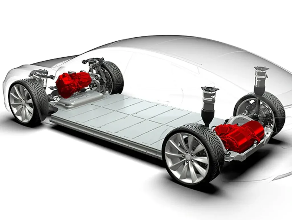 Obrázek zobrazuje technický nákres interiéru vozidla Tesla, konkrétně modelu Y. Je zde vidět průhledná karoserie vozidla, která odhaluje vnitřní komponenty. Baterie je umístěna na podvozku mezi přední a zadní nápravou. Přední a zadní elektromotory jsou zvýrazněny červenou barvou. Kromě baterií a motorů jsou viditelné i další části podvozku a systémů zavěšení kol, což demonstruje konstrukci a technickou sofistikovanost tohoto elektrického vozidla.