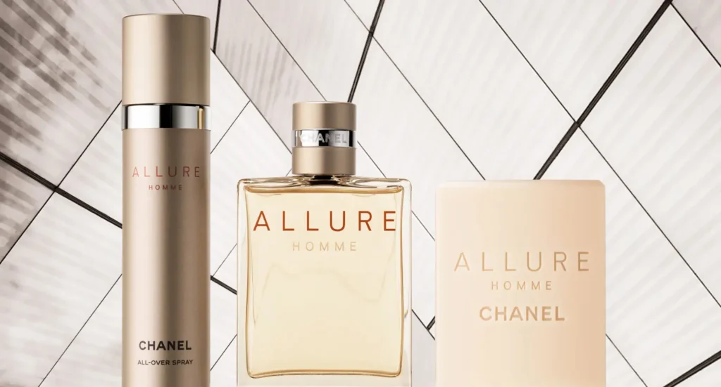 Fotografie tří produktů značky Chanel z řady Allure Homme. Zleva doprava se jedná o sprej All-Over Spray, parfémovou vodu a sprchový gel. Produkty jsou umístěny na pozadí s geometrickým vzorem v odstínech bílé a šedé.