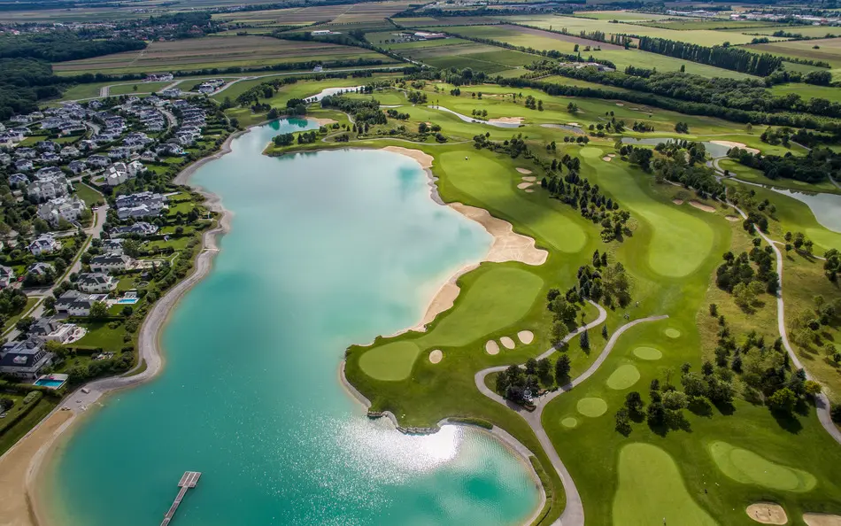 Letecký pohled na Fontana Golf Club v Rakousku, zobrazující rozsáhlé golfové hřiště obklopené jezerem a obytnou zástavbou.