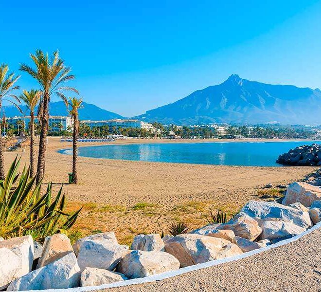 Pohled na nádhernou pláž v Marbelle na Costa del Sol ve Španělsku s modrým mořem, palmovými stromy a horským pozadím. Perfektní místo pro luxusní dovolenou plnou slunce a relaxace.