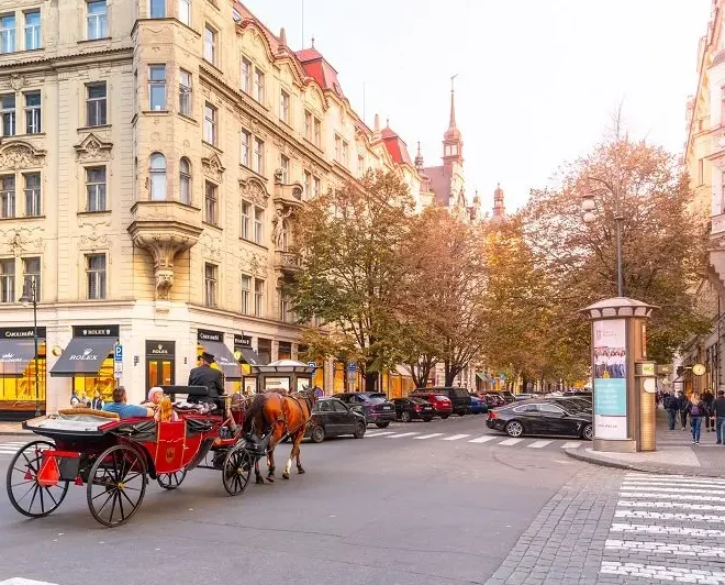 Pařížská ulice v Praze, pohled na elegantní historické budovy s luxusními butiky a projíždějící koňskou drožkou na křižovatce.