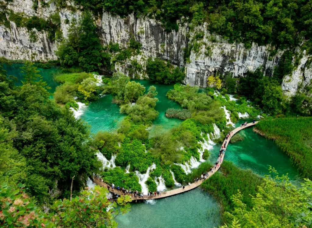 Turistická trasa v Plitvických jezerech v Chorvatsku, která vede přes dřevěný chodník nad tyrkysově modrými jezery obklopenými bujnou zelení a skalními útesy.