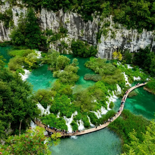 Turistická trasa v Plitvických jezerech v Chorvatsku, která vede přes dřevěný chodník nad tyrkysově modrými jezery obklopenými bujnou zelení a skalními útesy.