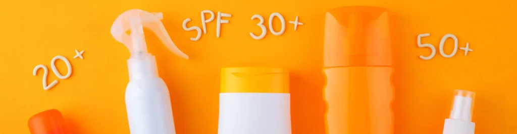 Lahvičky opalovacích krémů s ochranným faktorem SPF 20+, SPF 30+ a SPF 50+ na oranžovém pozadí.