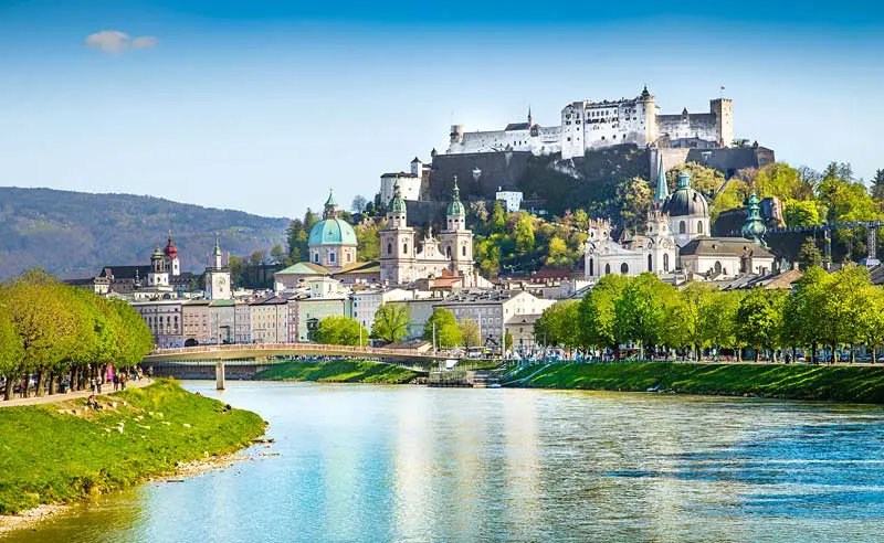 Panoramatický pohled na Salzburg v Rakousku s pevností Hohensalzburg na kopci a řekou Salzach v popředí.