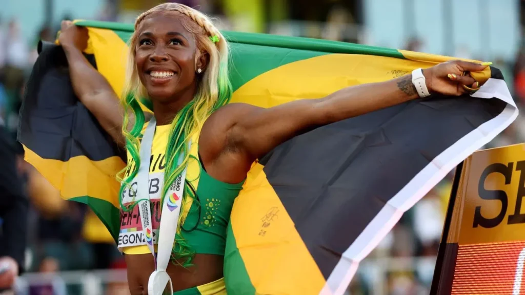 Jamajská sprinterka Shelly-Ann Fraser-Pryce oslavuje vítězství s jamajskou vlajkou na ramenou.