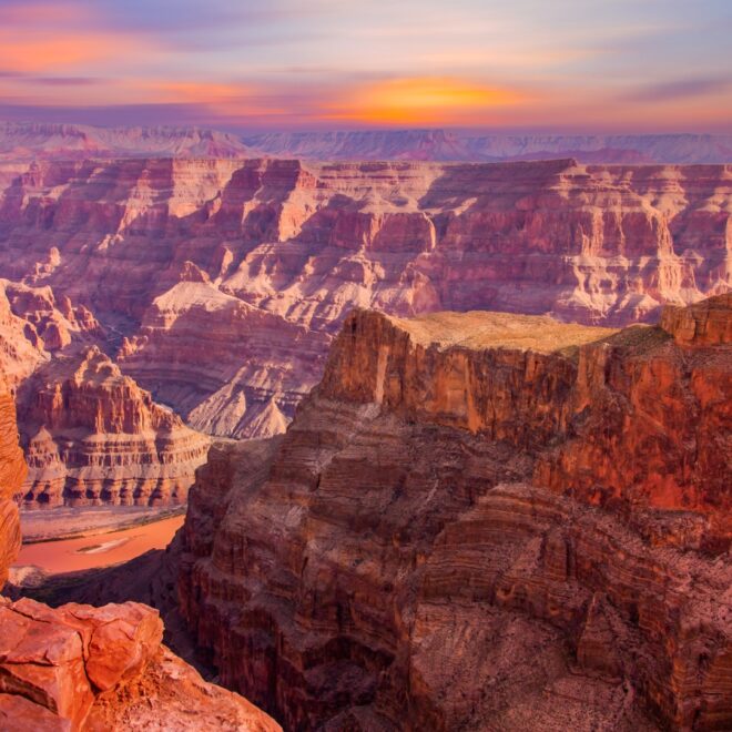 Pohled na Grand Canyon při západu slunce, kdy červené a oranžové vrstvy hornin září v měkkém světle a odhalují nádherné detaily geologických útvarů a hlubokých údolí.