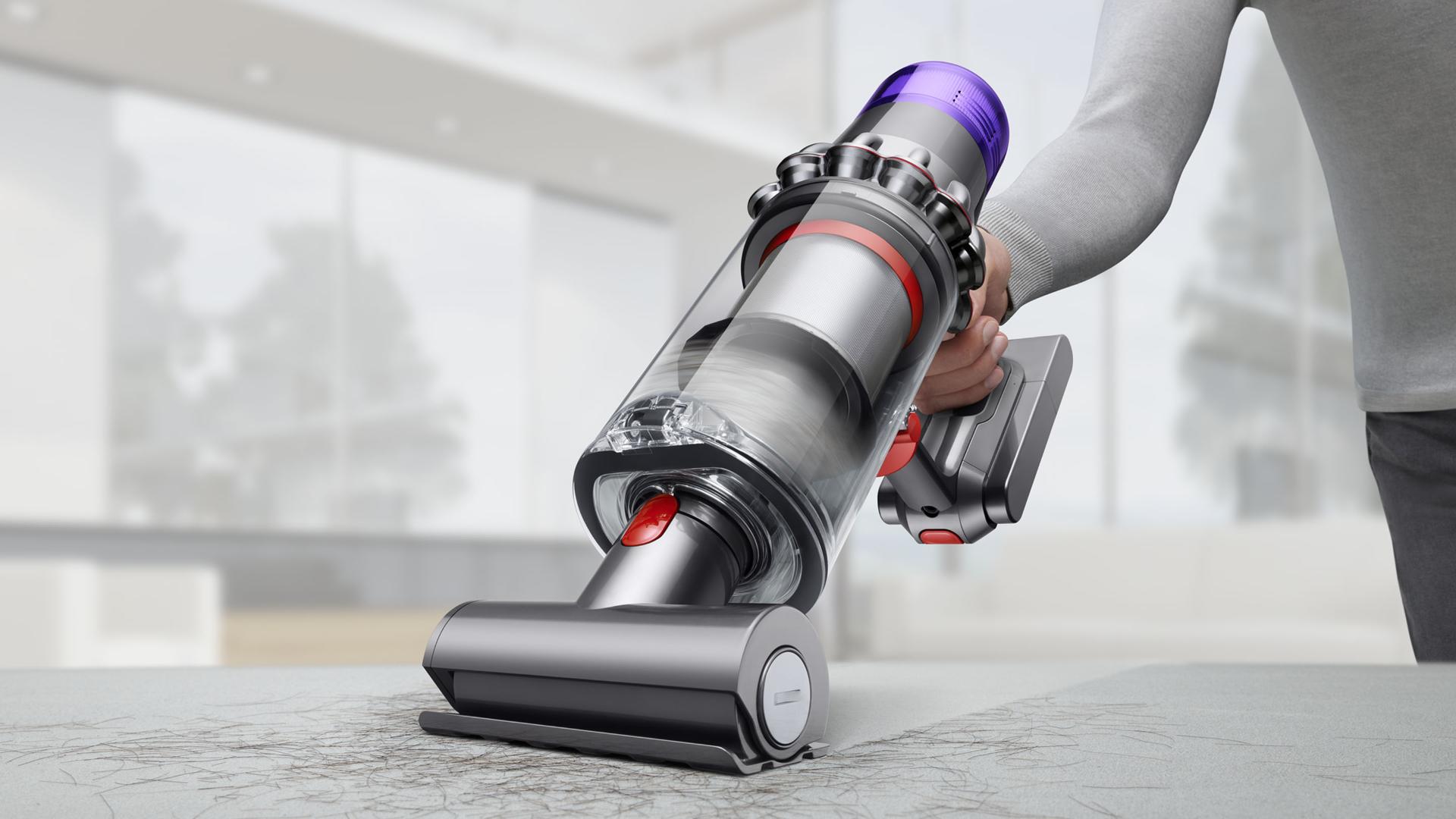 Tyčový vysavač Dyson V11 Absolute Extra Pro při vysávání chlupů na pohovce v moderní domácnosti.