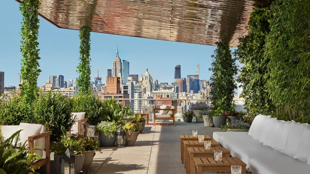 Luxusní rooftop bar v New Yorku s pohodlným posezením, zelení a úchvatným výhledem na panorama města, včetně ikonických mrakodrapů na Manhattanu.