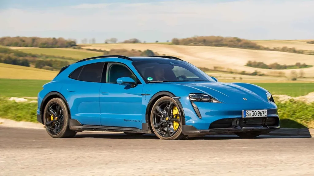 Modrý Porsche Taycan Turbo S projíždí venkovskou krajinou, ukazující svůj dynamický design a výjimečný výkon v kombinaci s elektrickou technologií.