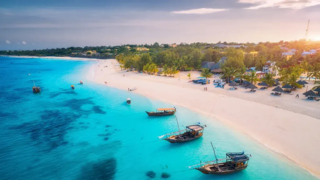 Malebná pláž na Zanzibaru s tradičními dřevěnými loďkami na tyrkysové vodě a bílým pískem.