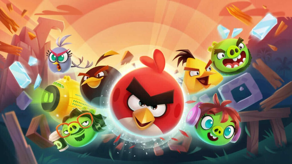 Ilustrace z videohry Angry Birds, zobrazující různé postavy, včetně červeného ptáka se zamračeným výrazem uprostřed, obklopeného jinými barevnými ptáky a zelenými prasaty v dynamickém a barevném prostředí s efekty energie a létajícími kusy dřeva.