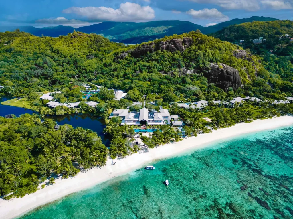 Letecký pohled na luxusní hotel obklopený tropickou vegetací na Seychelách s bílou písečnou pláží a tyrkysovou vodou.