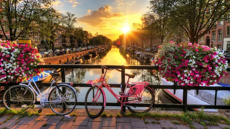 Krásný západ slunce nad amsterdamskými kanály s květinami a zaparkovanými bicykly.