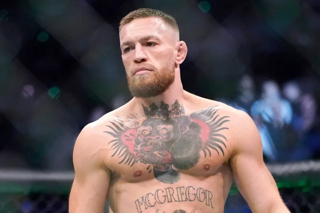 Conor McGregor, MMA bojovník, stojící v oktagonu během zápasu, s výrazným tetováním na hrudi, představující gorilu a nápis "McGregor