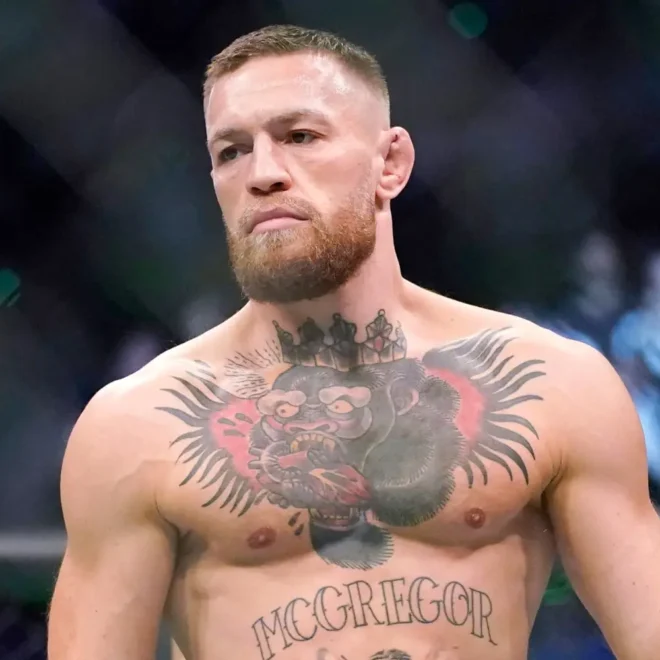 Conor McGregor, MMA bojovník, stojící v oktagonu během zápasu, s výrazným tetováním na hrudi, představující gorilu a nápis "McGregor