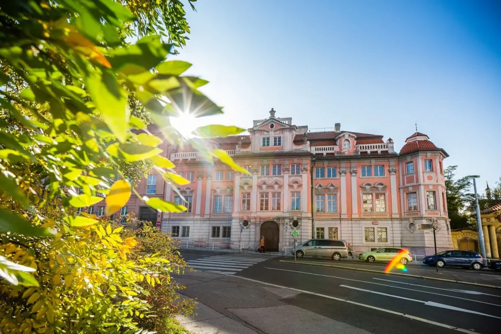 Barokní budova Faustova domu na Karlově náměstí za slunečného dne, obklopena listím. Dům je znám svou temnou historií a legendou o učenci Faustovi, kterého si měl odnést ďábel.