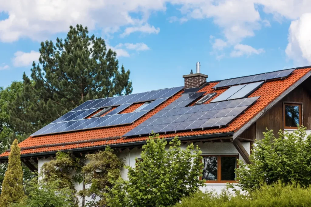 Fotovoltaické panely na střeše rodinného domu obklopeného zelení, sloužící k výrobě obnovitelné solární energie.