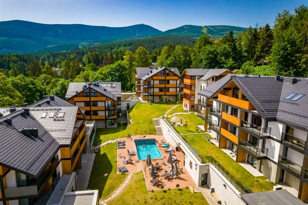 Hotel v polských Krkonoších, Karpacz, s moderními budovami a venkovním bazénem, obklopený nádhernou horskou krajinou a zelení.