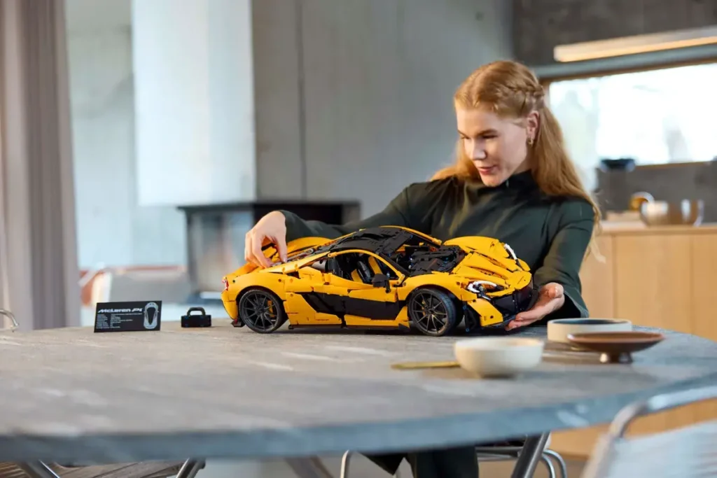 Žena sestavuje detailní model LEGO® Technic McLaren P1™ u stolu, soustředí se na pohyblivé části modelu.