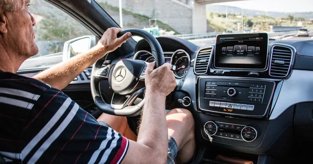 Muž řídící automobil značky Mercedes-Benz na dálnici, s jasně viditelným volantem a palubní deskou.