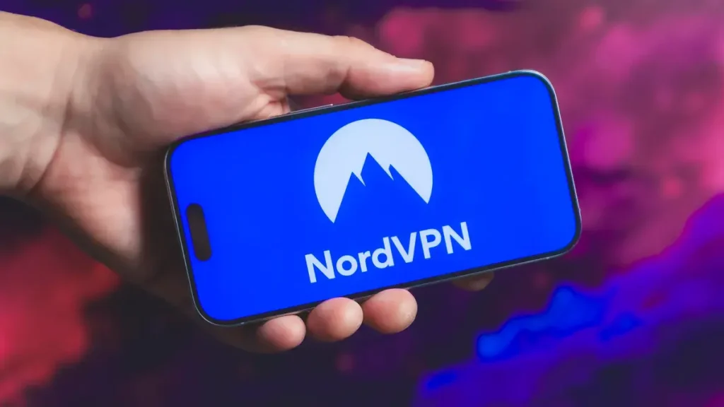 Ruka držící mobilní telefon s otevřenou aplikací NordVPN, zobrazující logo NordVPN na modrém pozadí.