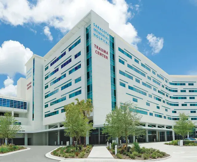 Nemocnice Sarasota Memorial Hospital - trauma centrum, moderní bílá budova s modrými okny obklopená zelení, s jasnou oblohou na pozadí.