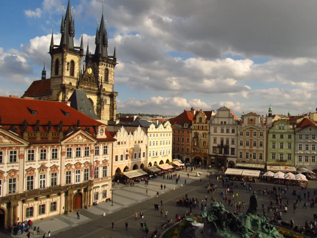 Staroměstské náměstí v Praze s Týnským chrámem a historickými domy, za oblačného dne s návštěvníky procházejícími po náměstí.