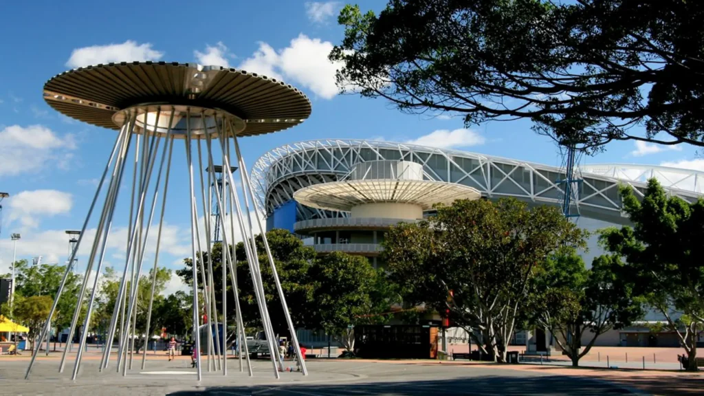 Sydney Olympic Park – moderní sportovní areál v Sydney obklopený zelení a zajímavými architektonickými prvky. Na fotografii jsou vidět ikonické konstrukce s kruhovými stínidly a stadion v pozadí, který byl hlavním centrem olympijských her v roce 2000.