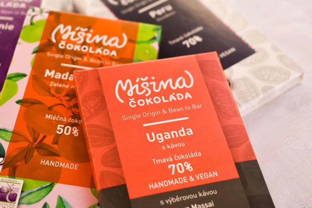 Různorodé tabulky Míšiny čokolády včetně tmavé čokolády Uganda 70 % s kávou a mléčné čokolády Madagaskar 50 %. Produkty jsou ručně vyráběné metodou bean to bar, s důrazem na kvalitu a původ surovin.