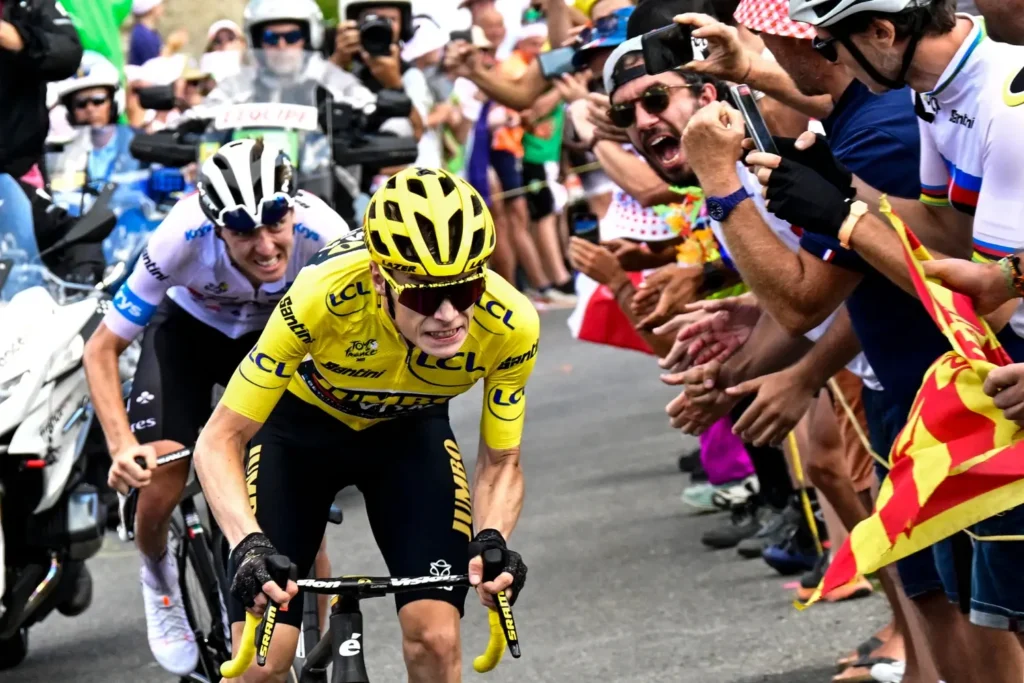 Cyklísta ve žlutém trikotu bojuje o vítězství během horské etapy na Tour de France, zatímco fanoušci hlasitě povzbuzují podél trasy.