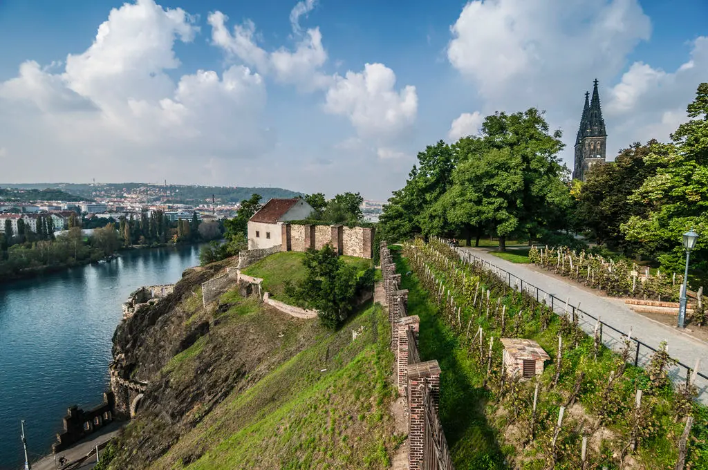 Vyšehrad v Praze, pohled na staré hradby, vinice a řeku Vltavu, s věží baziliky svatého Petra a Pavla v pozadí.