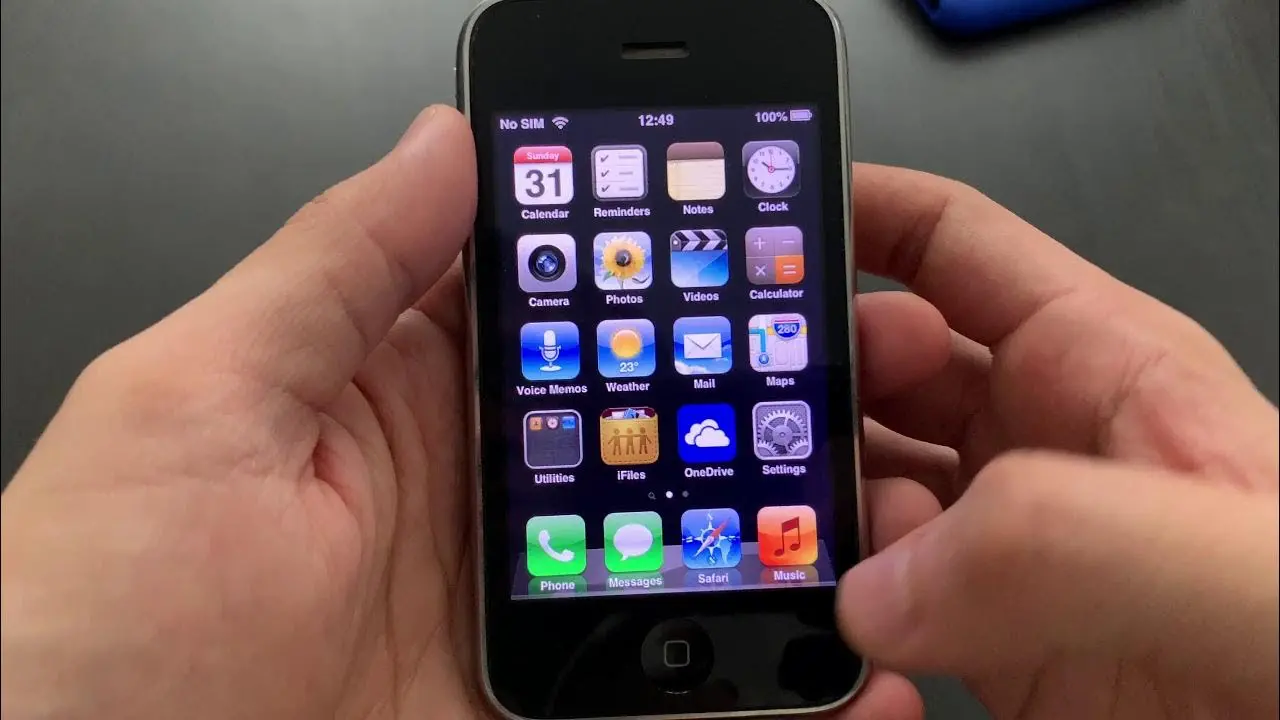 iPhone 3GS v ruce uživatele: Blízký pohled na iPhone 3GS v ruce, se zobrazením původního uživatelského rozhraní iOS s ikonickými aplikacemi, jako je Safari a Kamera.