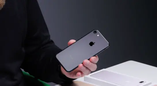 Černý iPhone 7 držený v ruce uživatele, zobrazující elegantní zadní část telefonu s lesklým povrchem a jedním fotoaparátem. Tento model se stal známým po odstranění 3,5mm sluchátkového jacku a přidání voděodolnosti.