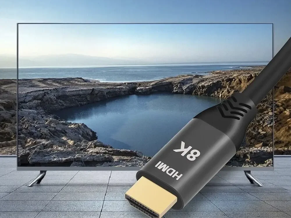 HDMI kabel podporující skutečné 8K rozlišení připojený k televizoru, který zobrazuje krajinu s jezerem a horami na obzoru.