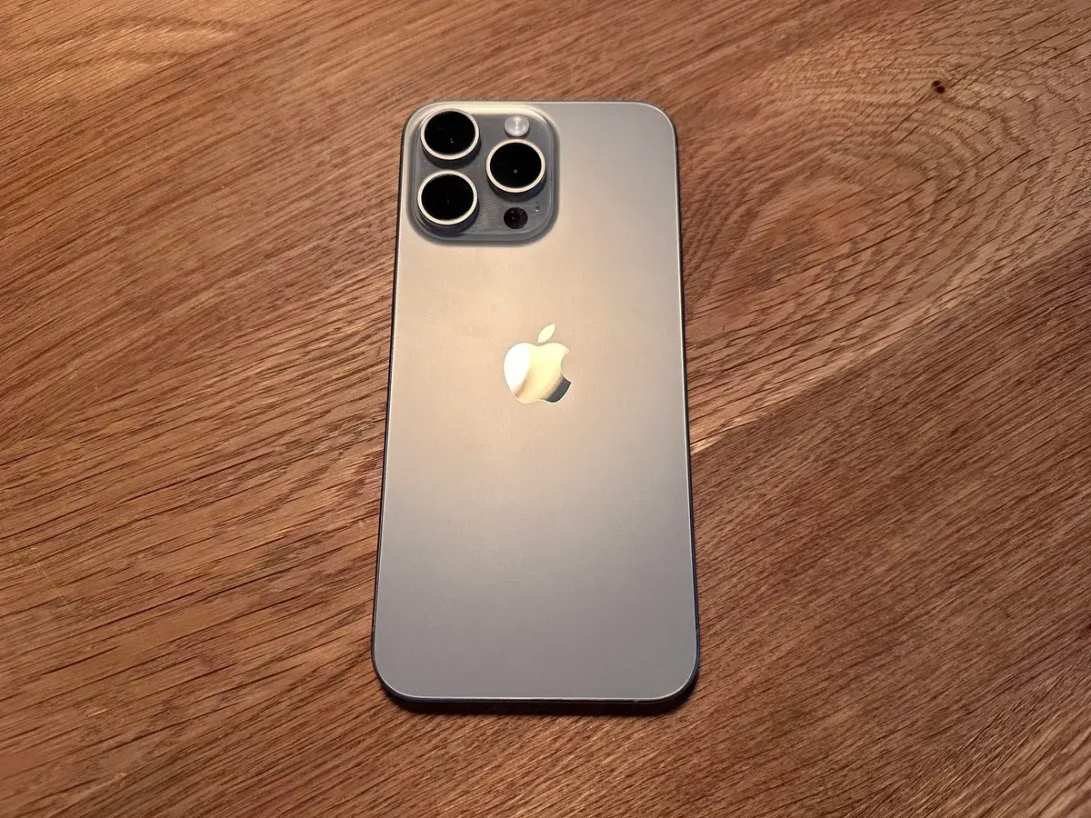 Zadní strana iPhone 16 Pro s třemi fotoaparáty na dřevěném stole