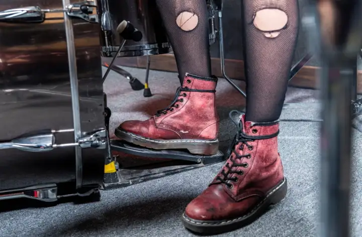 Červené boty Dr. Martens na nohou bubeníka hrajícího na bicí, kombinované s černými síťovanými punčochami.