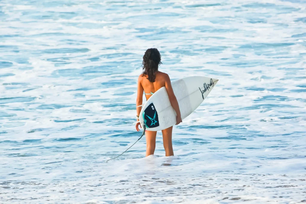 Surfařka s prknem stojí na břehu oceánu v Sayulitě, Mexiko, připravená vstoupit do vody a chytit vlny.