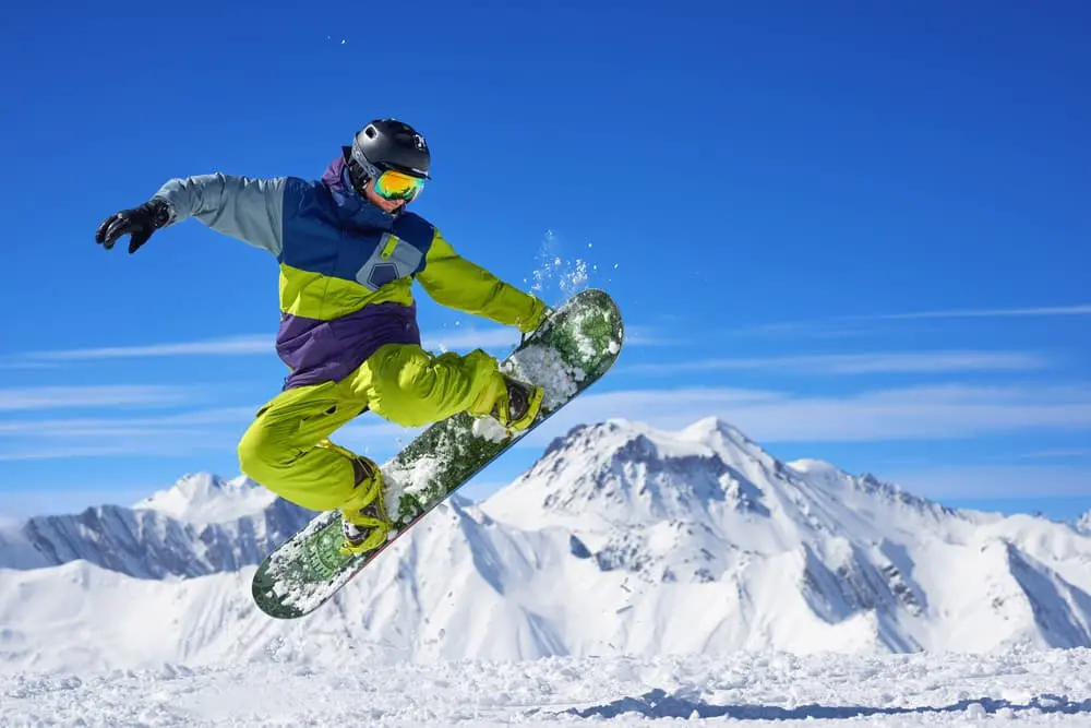 Snowboardista provádějící trik na sněhu s horami v pozadí.