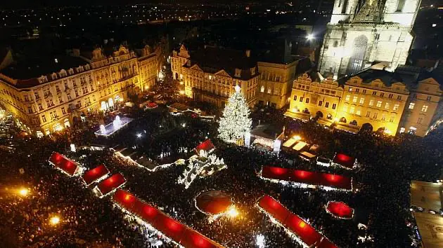 Vánoční trhy na Staroměstském náměstí v Praze v nočních hodinách, s osvětleným vánočním stromem a davy lidí kolem stánků.